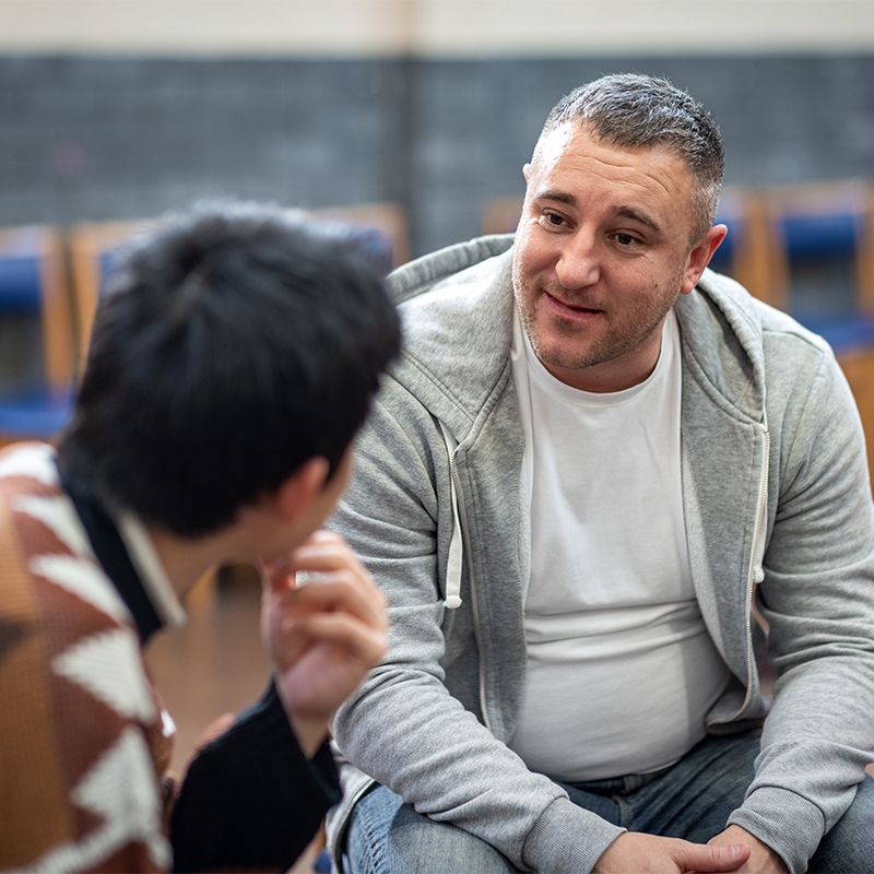Waist-up shot of two male adults sitting in a circle talking to each other about their mental well-being. They are all wearing casual clothing. The community centre is located in Seaton Deleval in the North East of England.